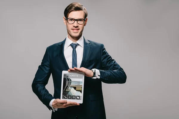 Homme d'affaires heureux tenant tablette numérique avec l'application de billets à l'écran isolé sur gris — Photo de stock