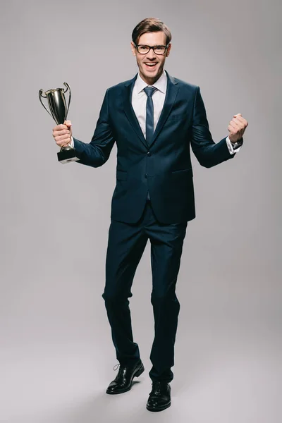 Schöner Geschäftsmann feiert Sieg und hält Trophäe in der Hand auf grauem Hintergrund — Stockfoto