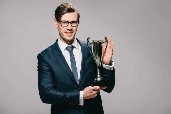 Bonito empresário segurando troféu em mãos isoladas em cinza — Fotografia de Stock