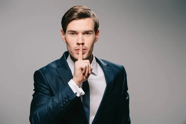 Guapo hombre de negocios poniendo el dedo en los labios sobre fondo gris - foto de stock