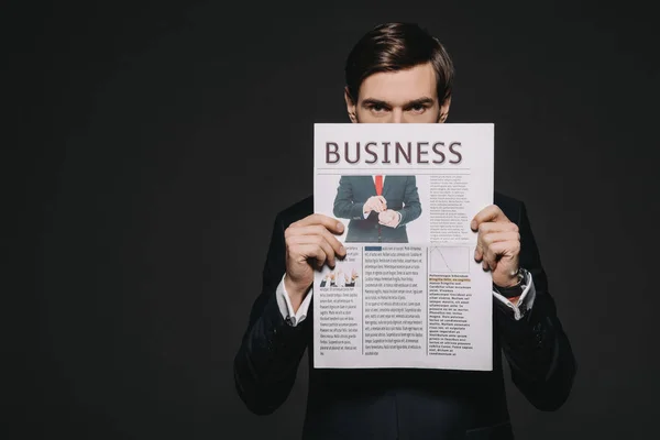 Businessman holding business newspaper in hands isolated on black — Stock Photo
