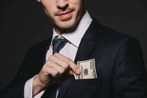 Vista recortada del hombre de negocios poniendo billete de dólar en el bolsillo aislado en negro - foto de stock