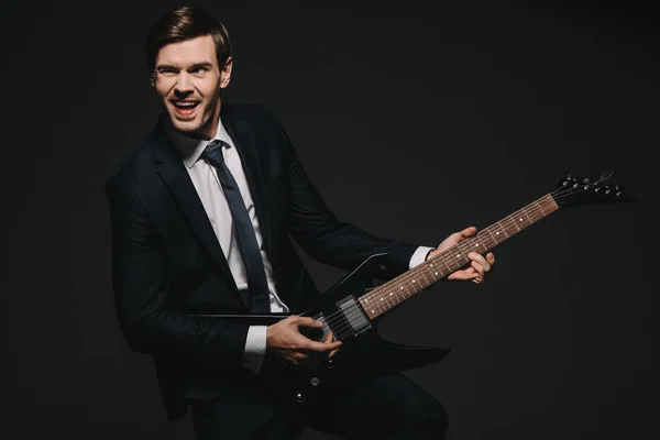 Cheerful businessman playing elecrtonic guitar isolated on black — Stock Photo