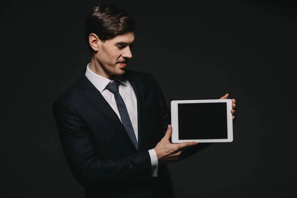 Alegre empresario sosteniendo tableta digital con pantalla en blanco aislado en negro - foto de stock