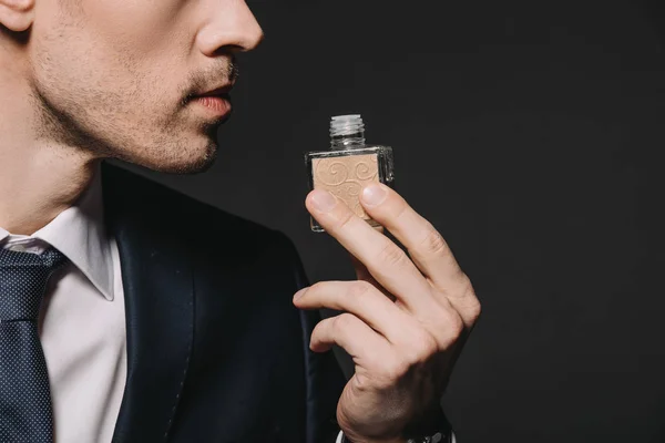 Vista recortada del hombre en traje oliendo perfume aislado en negro - foto de stock