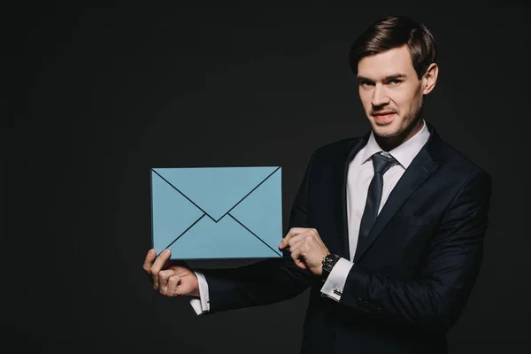 Bonito empresário segurando azul envelope isolado no preto — Fotografia de Stock