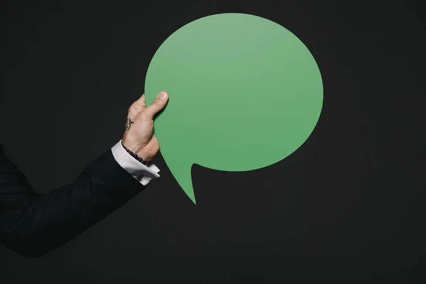 Обрізаний вид людини, що тримає зелену бульбашку мови в руках ізольовано на чорному — стокове фото
