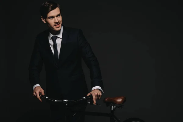 Fröhlicher Geschäftsmann im Anzug hält Fahrrad isoliert auf schwarzem Grund — Stockfoto
