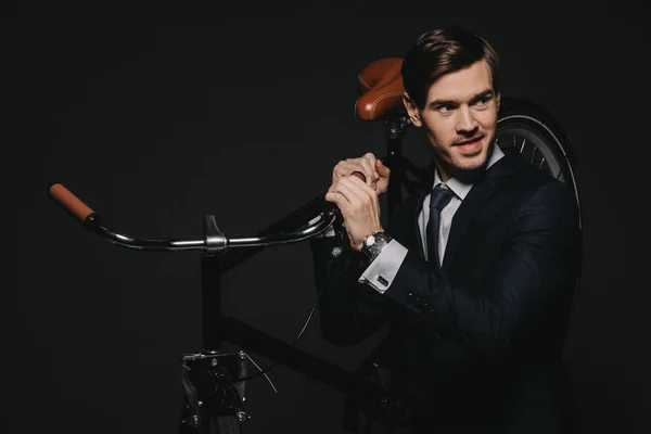 Красивий бізнесмен у костюмі тримає велосипед в руках ізольовано на чорному — стокове фото