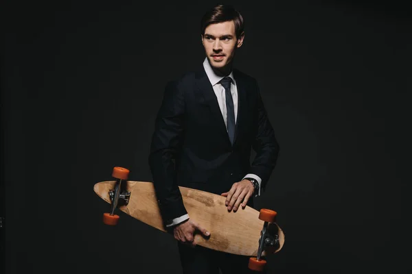Красивий бізнесмен тримає скейтборд в руках ізольовано на чорному — стокове фото