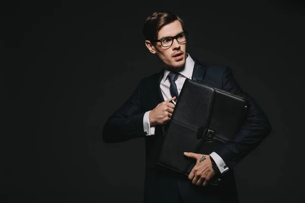 Hombre de negocios asustado en gafas con maletín en las manos aisladas en negro - foto de stock