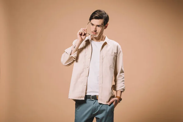 Homme confiant portant des lunettes et debout avec la main dans la poche isolé sur fond beige — Photo de stock