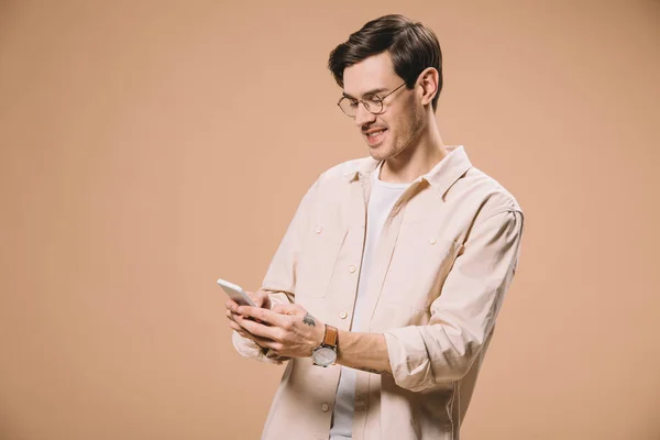 Веселий чоловік в окулярах дивиться на смартфон ізольовано на бежевому — стокове фото