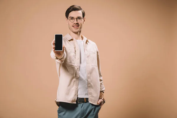 Homem bonito de pé com a mão no bolso e segurando smartphone com tela em branco isolado no bege — Fotografia de Stock