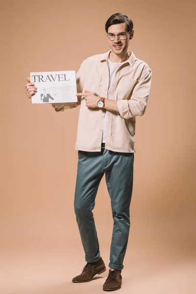 Uomo allegro che punta con il dito al giornale di viaggio su sfondo beige — Foto stock