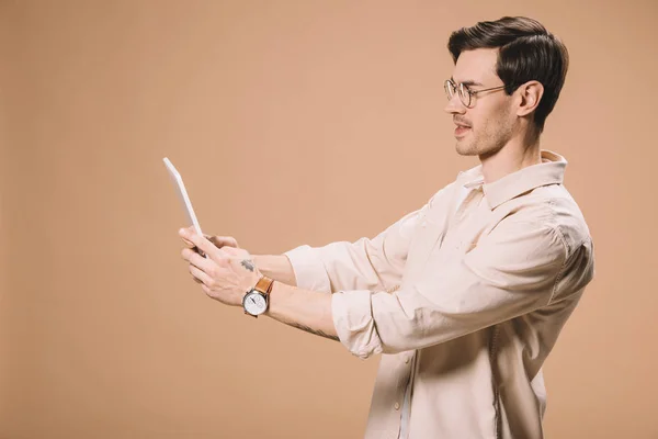 Hombre guapo en gafas usando tableta digital aislado en beige - foto de stock