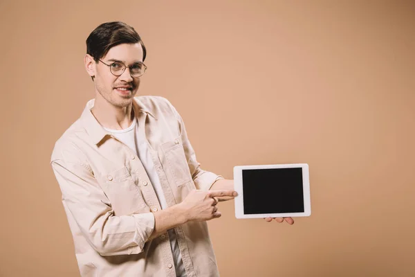 Lächelnder Mann mit Brille zeigt mit dem Finger auf digitales Tablet mit leerem Bildschirm, isoliert auf beige — Stockfoto