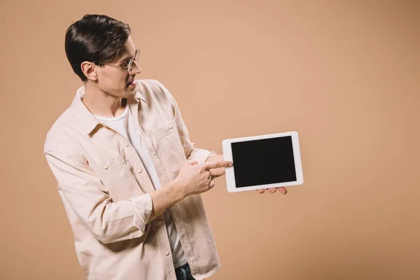 Hombre en gafas apuntando con el dedo a la tableta digital con pantalla en blanco aislado en beige - foto de stock