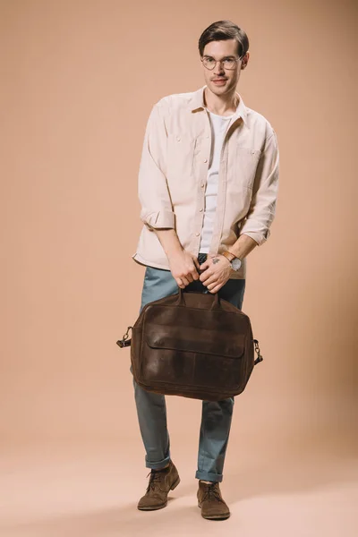 Красивый мужчина в очках с коричневой сумкой на бежевом фоне — стоковое фото
