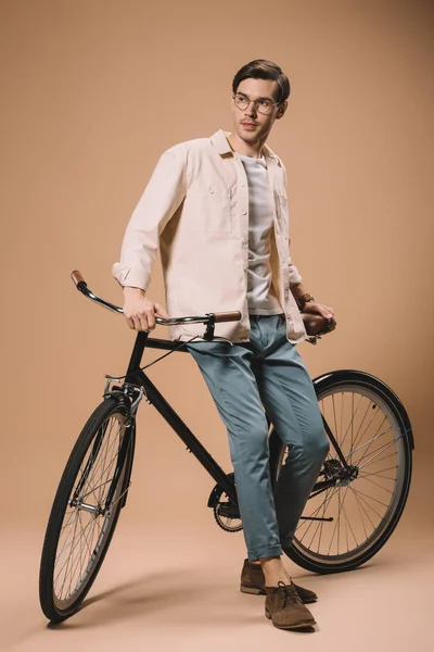 Bel homme en lunettes debout près du vélo sur fond beige — Stock Photo