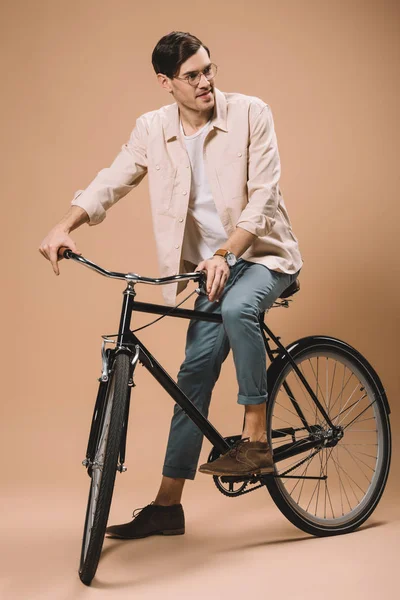 Cheerful man in glasses riding bike on beige background — Stock Photo