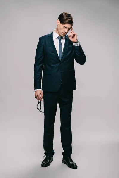 Handsome businessman standing in suit and holding head on grey background — Stock Photo