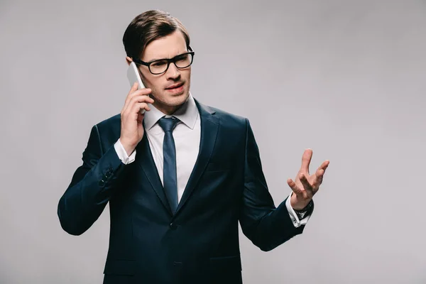 Schöner Geschäftsmann mit Brille, der auf dem Smartphone spricht, während er im Anzug isoliert auf grau steht — Stockfoto