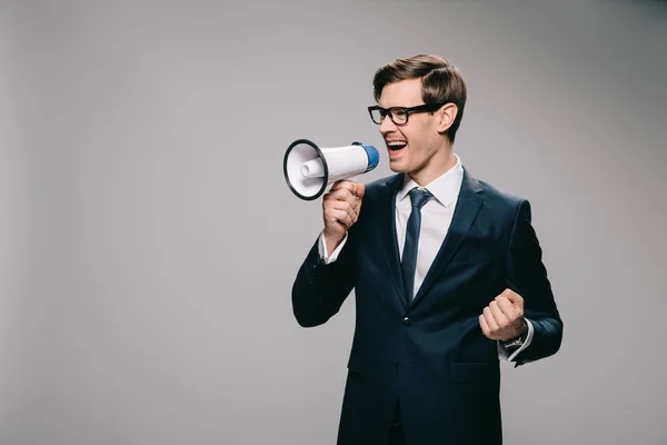 Glücklicher Geschäftsmann schreit in Megafon vor grauem Hintergrund — Stockfoto