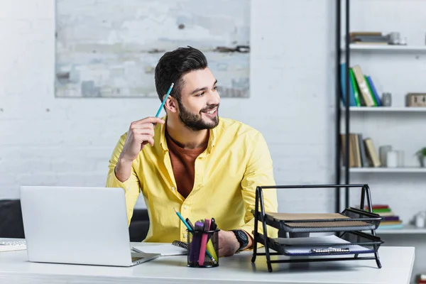 Empresário sorridente segurando lápis e olhando para a mesa de madeira — Fotografia de Stock