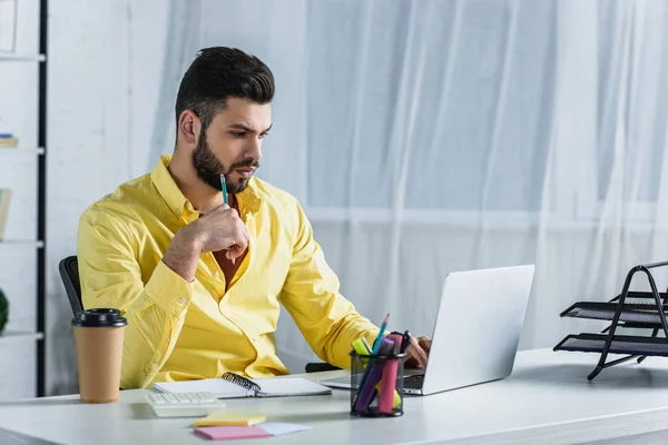 Konzentrierter bärtiger Geschäftsmann blickt auf Laptop-Bildschirm und hält Bleistift in der Hand — Stockfoto