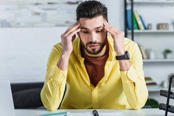 Homme d'affaires barbu réfléchi en chemise jaune touchant la tête sur le lieu de travail — Photo de stock