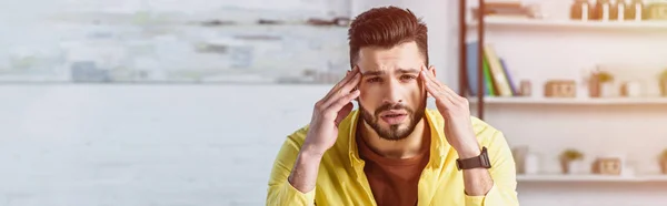 Sad businessman in yellow shirt touching head and looking at camera — Stock Photo