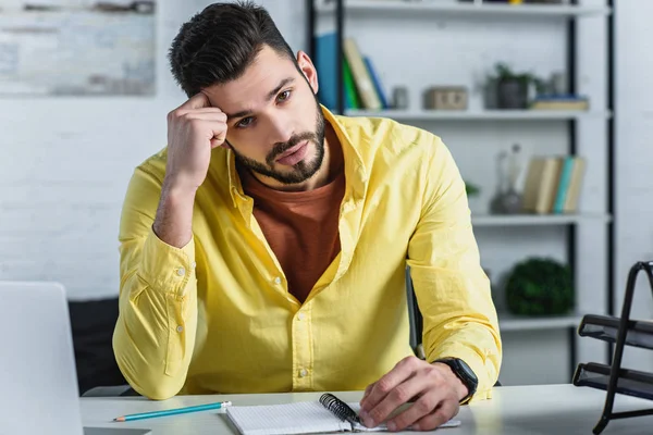 Concentrated businessman in yellow shirt looking at camera and touching head — Stock Photo