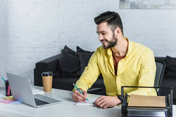 Empresário sorrindo usando laptop e escrevendo em notebook — Fotografia de Stock