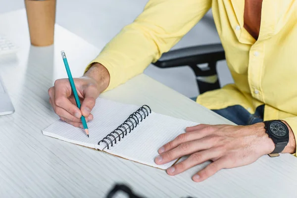 Ausgeschnittene Ansicht eines Mannes, der am Schreibtisch in Notizbuch schreibt — Stockfoto