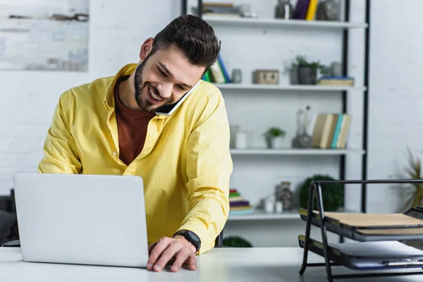 Homme d'affaires barbu souriant en chemise jaune parlant sur smartphone au bureau — Photo de stock