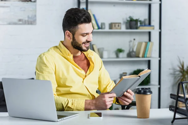 Lächelnder bärtiger Geschäftsmann im gelben Hemd liest Buch im Büro — Stockfoto