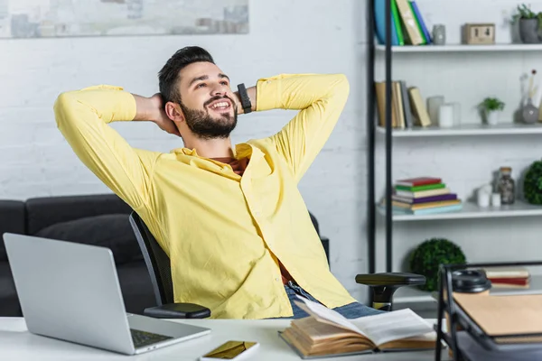 Hombre de negocios barbudo sonriente con camisa amarilla con brazos cruzados mirando hacia el lugar de trabajo - foto de stock