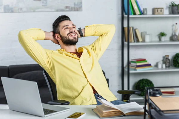 Lächelnder bärtiger Geschäftsmann im gelben Hemd mit verschränkten Armen, der zum Arbeitsplatz aufschaut — Stockfoto