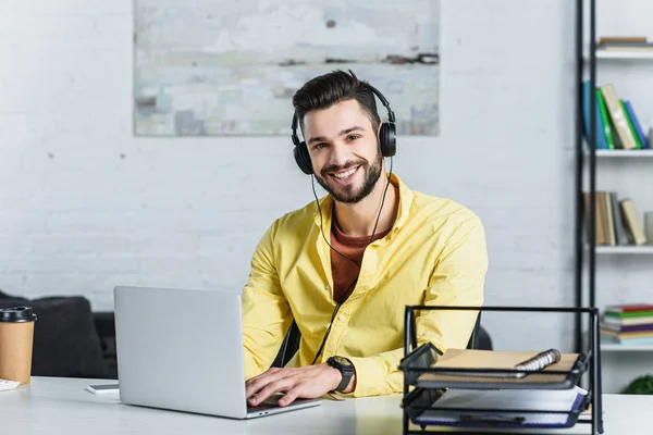 Smiling bearded businessman listening to music and looking at camera at office — Stock Photo