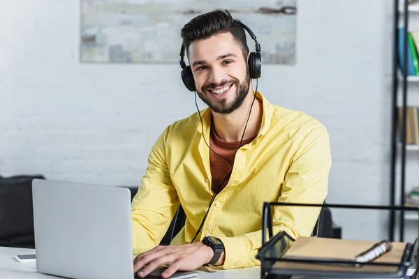 Homme d'affaires barbu joyeux avec écouteurs regardant la caméra au bureau — Photo de stock