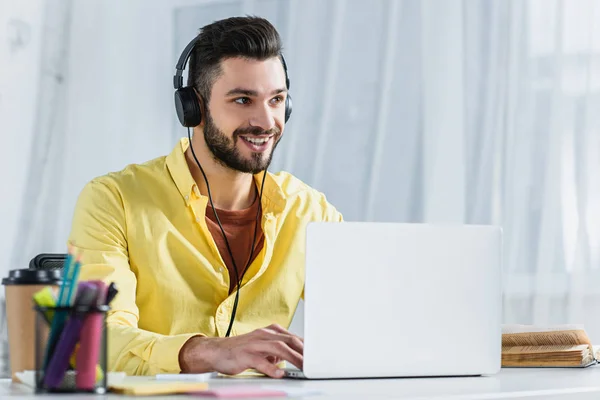 Smiling bearded businessman in headphones looking away at workplace — Stock Photo