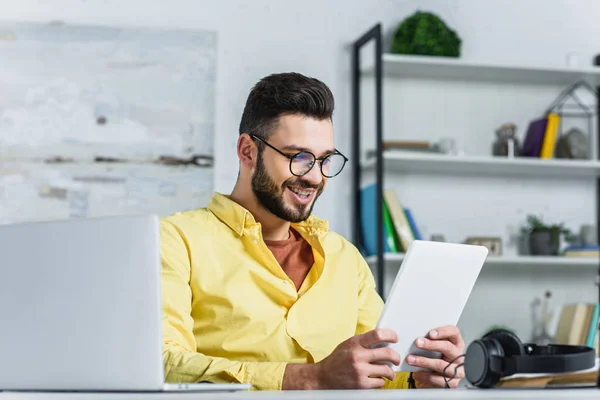 Усміхнений бородатий бізнесмен в окулярах дивиться на планшетний екран в офісі — стокове фото