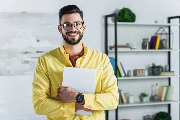 Uomo d'affari sorridente in occhiali che tengono il tablet digitale e guardano la macchina fotografica a ufficio — Foto stock