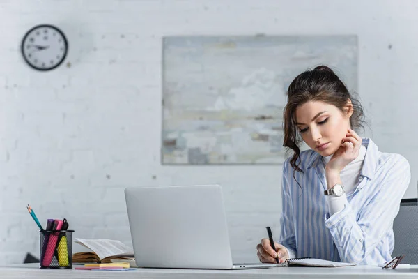Focused attractive businesswoman writing in notebook at workplace — Stock Photo