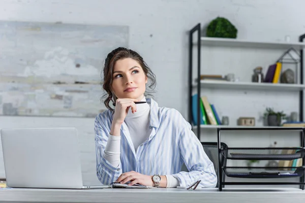 Femme d'affaires réfléchie tenant un stylo et regardant loin sur le lieu de travail — Photo de stock