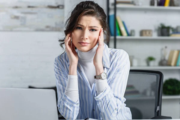 Upset attractive businesswoman touching head and  looking at camera at workplace — Stock Photo