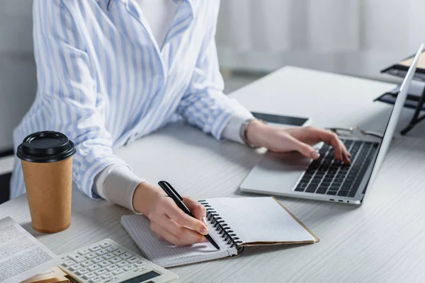 Cropped view of woman writing in notebook on wooden desk — Stock Photo