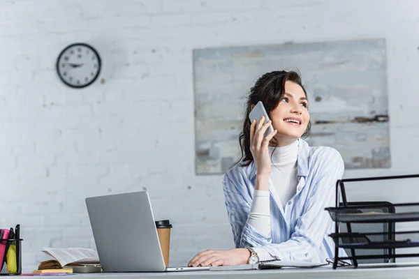 Hermosa mujer de negocios hablando en el teléfono inteligente y mirando hacia la oficina - foto de stock