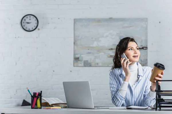 Atractiva empresaria sosteniendo una taza de papel y hablando en un teléfono inteligente - foto de stock